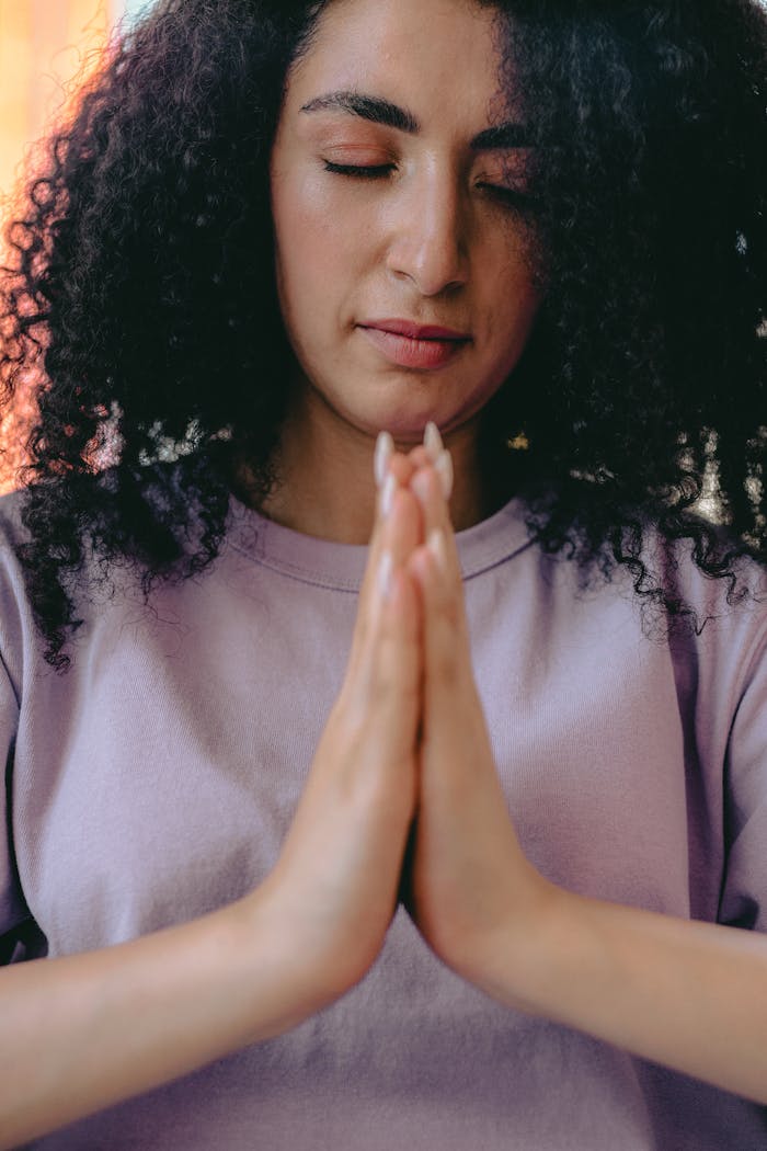 service-03 Young woman with curly hair meditating indoors with hands in prayer.