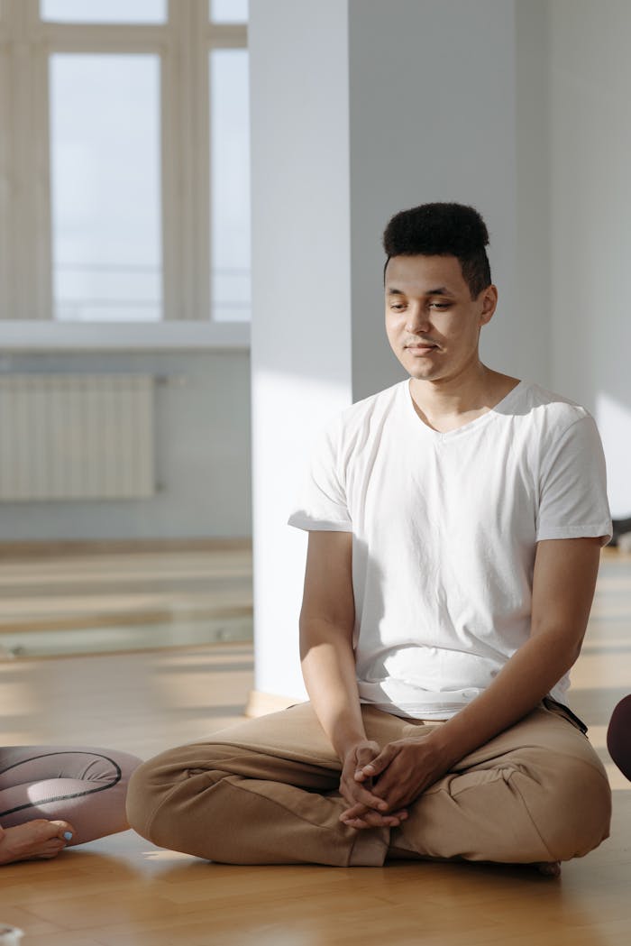 Adult man practicing meditation sitting on the floor in a sunlit indoor space, promoting relaxation and mindfulness.