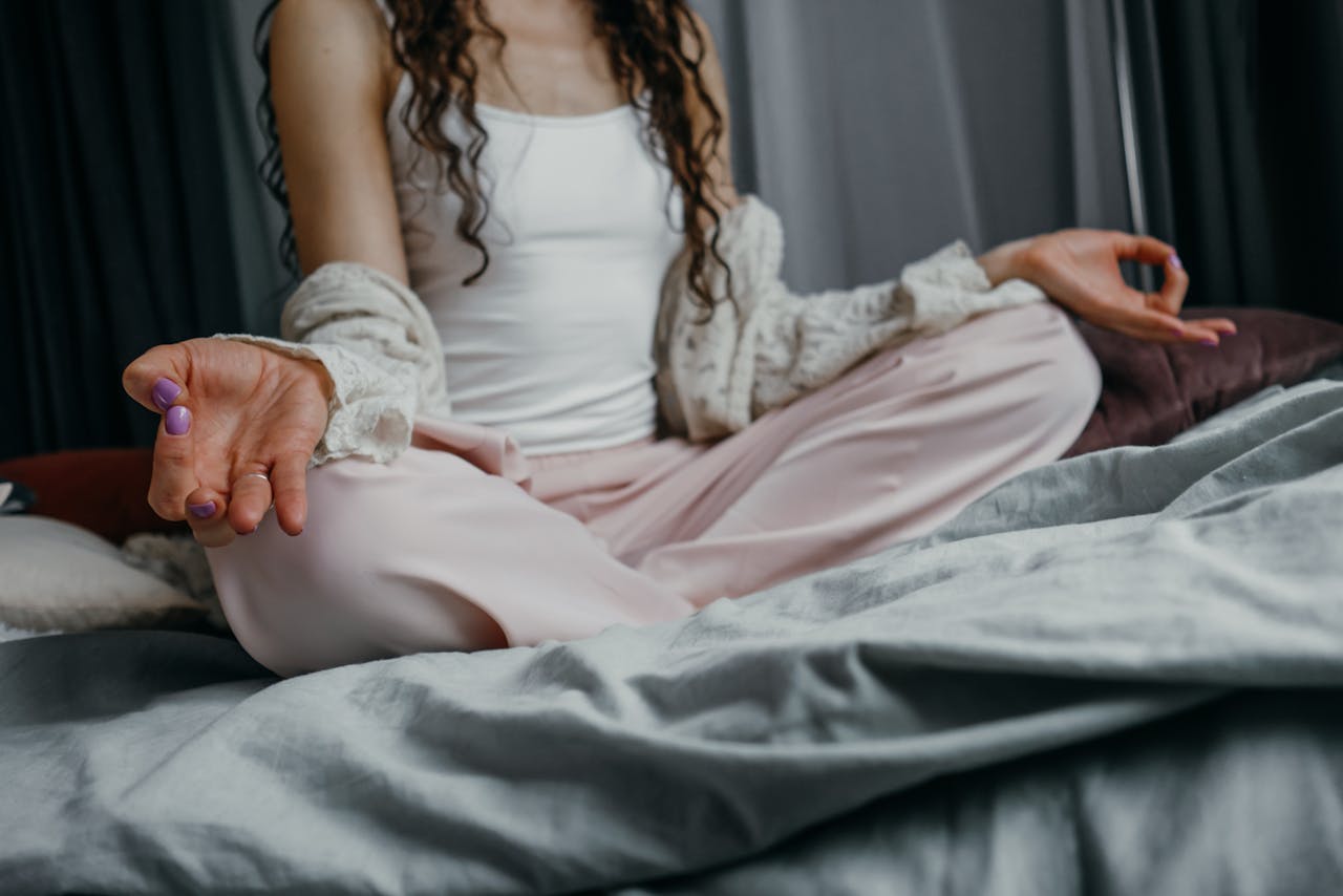 A woman practicing yoga meditation on her bed, promoting a peaceful and healthy lifestyle.