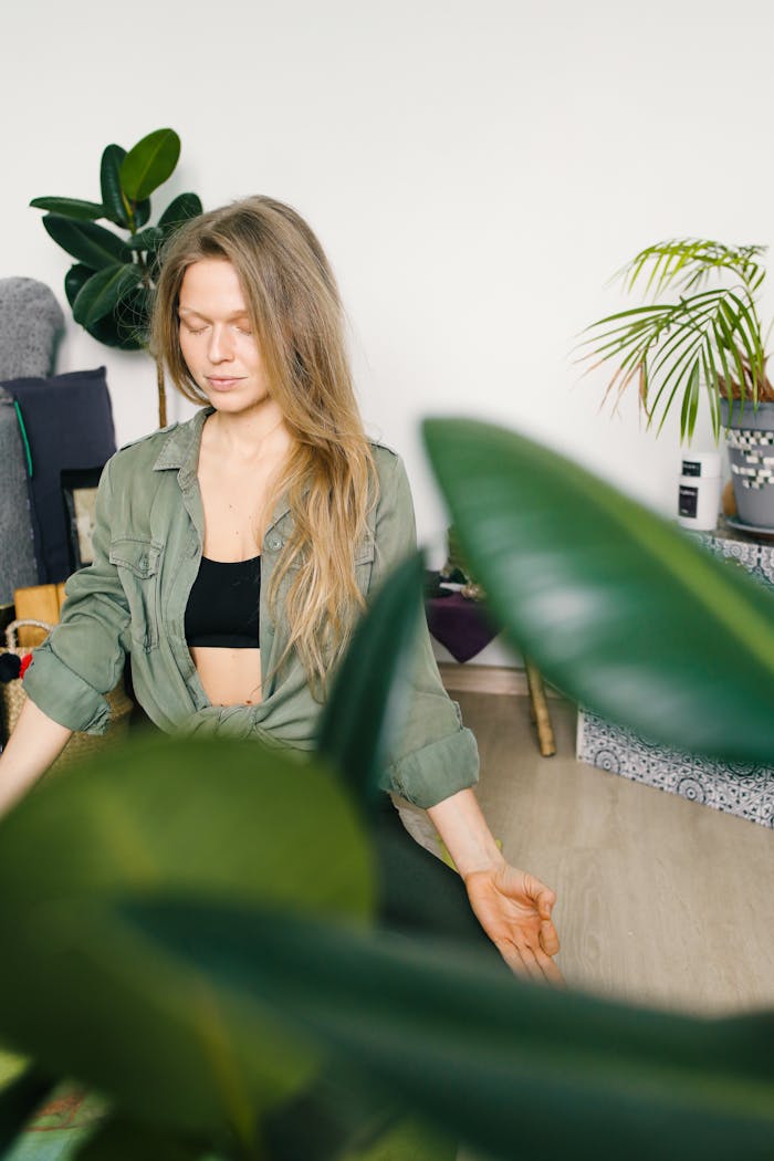 service-02 Woman practicing meditation indoors surrounded by greenery, eyes closed for focus and relaxation.